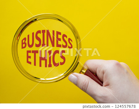 Business ethics symbol. Concept word Business ethics on magnifying glass. Businessman hand. Beautiful yellow background. Business and Business ethics concept. Copy space 124557678