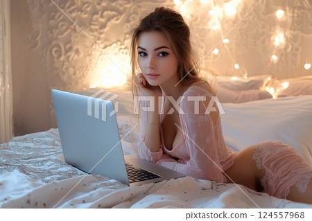 Sexy young woman in lingerie with a laptop on the bed broadcasts online for subscribers. Working in adult entertainment industry from home remotely. Sex webcam model, online dating app 124557968