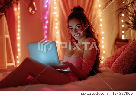 Sexy young woman in lingerie with a laptop on the bed broadcasts online for subscribers. Working in adult entertainment industry from home remotely. Sex webcam model, online dating app 124557969