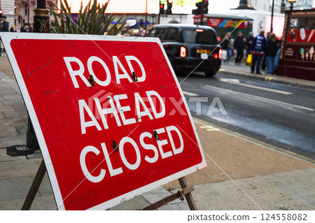 Temporary Road Ahead Closed Sign Placed on Sidewalk with City Traffic 124558082
