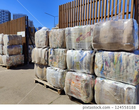 Large bundles of compressed paper waste, wrapped in plastic, waiting to be processed at an urban recycling plant. 124558188