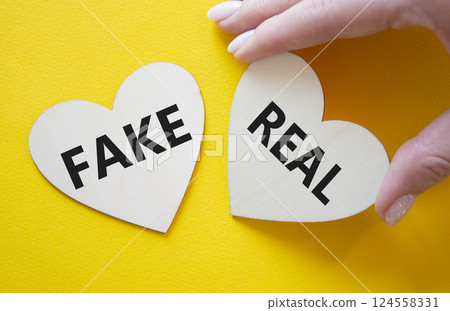 Real or Fake symbol. Concept word Real or Fake on wooden hearts. Businessman hand. Beautiful yellow background. Business and Real or Fake concept. Copy space 124558331