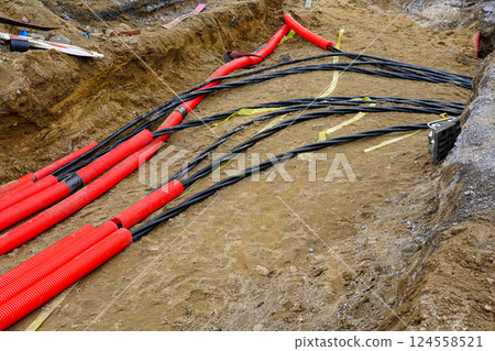 Laying new underground high-voltage power cable in red corrugated protective tube Laying new underground high-voltage power cable in red corrugated protective tube 124558521