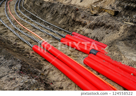 Laying new underground high-voltage power cable in red corrugated protective tube Laying new underground high-voltage power cable in red corrugated protective tube 124558522