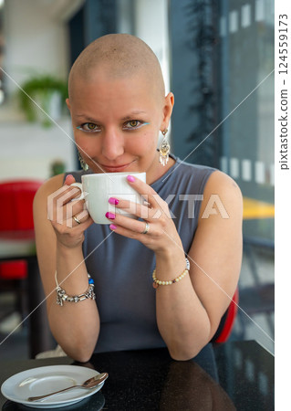 Young woman with cancer sitting in a cafe, drinking coffee and enjoying everyday life. The concept highlights that people with illnesses continue to live actively and socialize 124559173