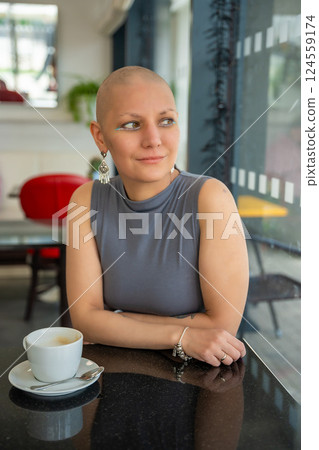 Young woman with cancer sitting in a cafe, drinking coffee and enjoying everyday life. The concept highlights that people with illnesses continue to live actively and socialize 124559174