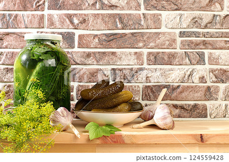 Pickled cucumbers in a plate and a jar of pickles with garlic and dill on a wooden kitchen table, rustic harvest, homemade pickling recipe, cucumbers and ingredients for pickling, home canning Pickled cucumbers in a plate and a jar of pickles with garlic and dill on a wooden kitchen table, rustic harvest, homemade pickling recipe, cucumbers and ingredients for pickling, home canning 124559428