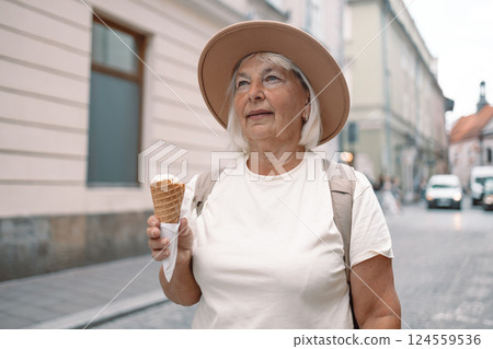 Senior woman walking down the street with an ice cream cone in hand, enjoying the moment. Senior woman walking down the street with an ice cream cone in hand, enjoying the moment. 124559536
