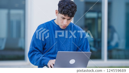 Focused student working on laptop outside university building Focused student working on laptop outside university building 124559689