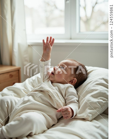 Cozy morning with curious baby reaching for light in soft white bedroom environment 124559861