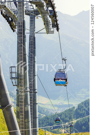 Scenic cable car glides lush valley with towering metal columns along scenic Grossglockner Alps Tyrol valley mountains. Panoramic view  sweeping alpine vistas stunning journey high above terrain 124560007