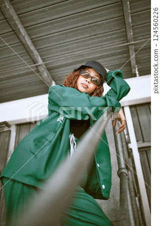 Fashion, street style and woman with green clothes, sunglasses and hat standing on stairs of an urban city building. Portrait of a cool female, hip hop or fashionable hipster model with casual outfit 124560226