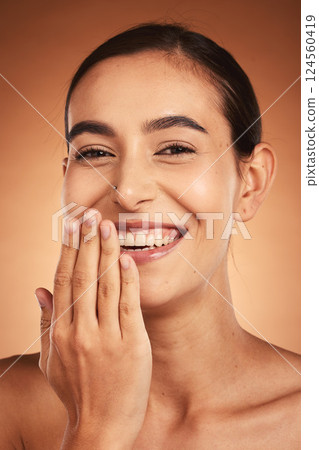 Skincare, hand and woman in studio for skin, makeup and beauty on orange background, happy and relax. Hand, portrait and face of indian wellness model smile for secret, cosmetic and product mockup 124560419