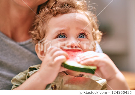 Baby, water melon and cute with an infant boy child eating fruit with his mother in the home together. Food, health and summer with a young kid biting a piece of watermelon with his mom in a house 124560435