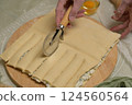 Close up square sheet of dough cut into strips with woman's hands on wooden board. Cutter, egg on kitchen table. Home cooking baking puffs 124560564