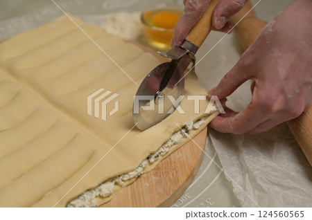 Close up square sheet of dough cut into strips with woman's hands on wooden board. Cutter, flour, egg on kitchen table. Home cooking baking puffs Close up square sheet of dough cut into strips with woman's hands on wooden board. Cutter, flour, egg on kitchen table. Home cooking baking puffs 124560565