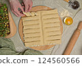 Top view woman's hands twists dough strips on wooden board. Cutter, egg, green towel, microgreens sprouts on kitchen table. Home cooking baking puffs 124560566