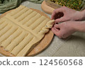 Close up woman's hands twists dough strips on wooden board. Green towel, microgreens sprouts on kitchen table. Home cooking baking puffs 124560568