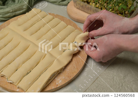 Close up woman's hands twists dough strips on wooden board. Green towel, microgreens sprouts on kitchen table. Home cooking baking puffs 124560568