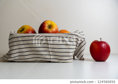 A basket of apples covered by a tea towel with an apple next to the basket on a white background 124560850