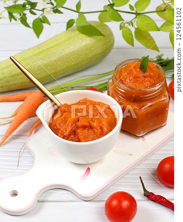 Zucchini caviar with ingredients for cooking on a concrete table, the concept of home canning and harvesting vegetables, healthy organic food, tomatoes, zucchini, carrots and peppers on the kitchen 124561102