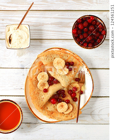 Delicious Russian pancakes with soft curd cheese, bananas, cranberries and honey on a wooden table. Healthy breakfast with ingredients, carnival concept and traditional national cuisine, selective 124561251