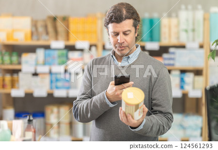 Male shopper in autumn clothes scans QR code on label of food for small children using smartphone 124561293