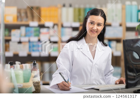 Woman pharmacy employee works with computer and notebook dairy. 124561317