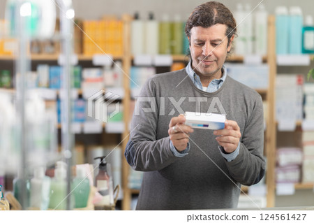 Man choose antifungal ointment in pharmacy, examine packaging 124561427