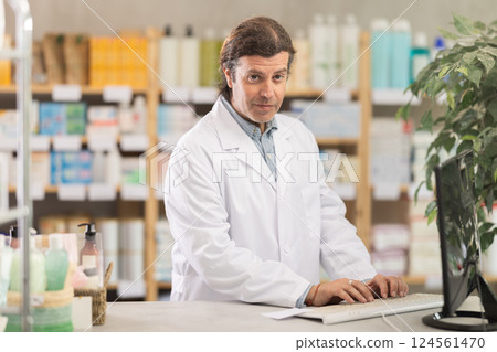 Pharmacist in uniform looking for medicine in pharmacy using computer Pharmacist in uniform looking for medicine in pharmacy using computer 124561470