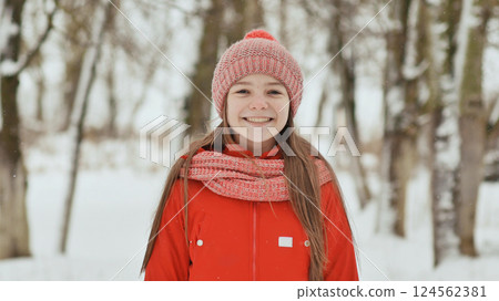 A teenage girl with freckles on her face happily smiles into the camera. A background of a winter forest landscape. A teenage girl with freckles on her face happily smiles into the camera. A background of a winter forest landscape. 124562381