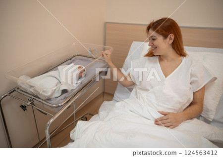 A young mother admires her newborn son in the maternity hospital. A young mother admires her newborn son in the maternity hospital. 124563412