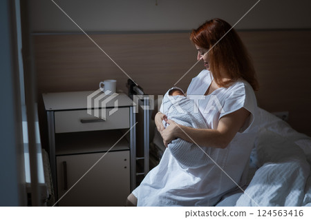 Caucasian woman holding newborn son while sitting on couch in maternity hospital ward.  124563416