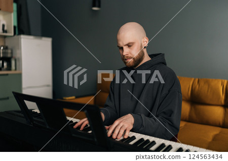 Concentrated male musician plying on electric piano, composing music at home, practicing and recording new song in stylish modern apartment setting. Concept of recording music at home. 124563434