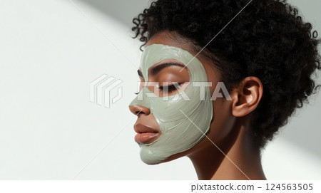 A minimalist photo of a dark-skinned woman with short curly hair applying a facial mask 124563505