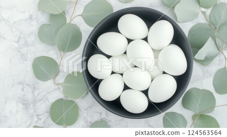 Elevate Easter celebrations with a minimalist Easter centerpiece featuring elegant white Easter eggs surrounded by delicate eucalyptus leaves on a marble countertop 124563564