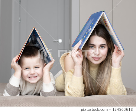 Concept home, family. Beautiful 19 year old girl and 5 year old boy lying on bed holding books above their heads in shape of house. Concept home, family. Beautiful 19 year old girl and 5 year old boy lying on bed holding books above their heads in shape of house. 124563618