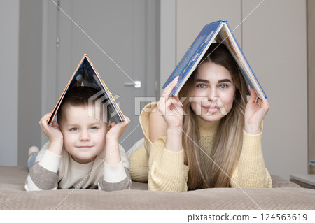 Concept home, family. Beautiful 19 year old girl and 5 year old boy lying on bed holding books above their heads in shape of house. Concept home, family. Beautiful 19 year old girl and 5 year old boy lying on bed holding books above their heads in shape of house. 124563619