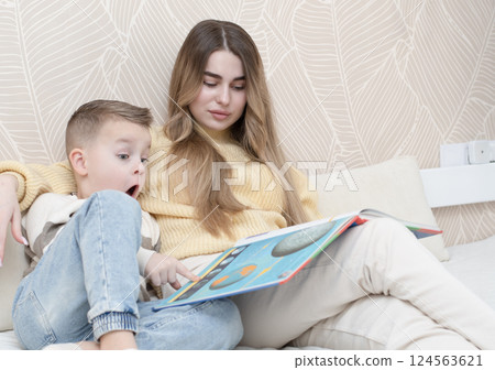 Concept family. Beautiful 19 year old girl and 5 year old boy are sitting on the bed in the children's room and reading a book together. Demonstrating a common moment of learning and togetherness. 124563621