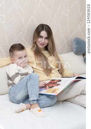 Concept family. Beautiful 19 year old girl and 5 year old boy are sitting on the bed in the children's room and reading a book together. Demonstrating a common moment of learning and togetherness. 124563628