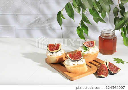 Healthy breakfast with ingredients, toast with figs and soft cream cheese ricotta and honey, canapes or crostini with toasted baguette and herbs on a light sunny table, Italian recipe menu, selective 124564007