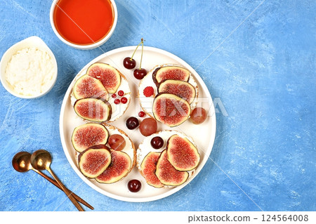 Ricotta,figs and bruschetta with honey on blue marble.Fresh sandwiches and toast with cream cheese,sliced figs,honey and cherries.Healthy breakfast with ingredients,lunch or dessert,diet food 124564008
