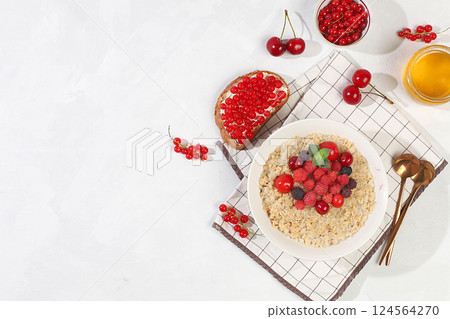 Healthy breakfast with ingredients, oatmeal pudding or porridge with raspberries, cherries, currants, honey and toast on a sunny table. The concept of healthy and natural food, lifestyle, food for 124564270