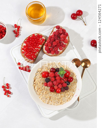 Healthy breakfast with ingredients, oatmeal pudding or porridge with raspberries, cherries, currants, honey and toast on a sunny table. The concept of healthy and natural food, lifestyle, food for Healthy breakfast with ingredients, oatmeal pudding or porridge with raspberries, cherries, currants, honey and toast on a sunny table. The concept of healthy and natural food, lifestyle, food for 124564271