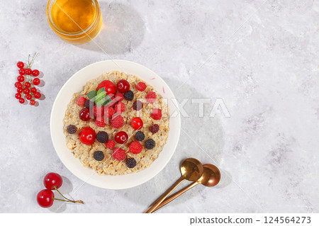 Healthy breakfast with ingredients, oatmeal pudding or porridge with raspberries, cherries, currants, honey on a sunny table. The concept of healthy and natural food, lifestyle, food for children, 124564273