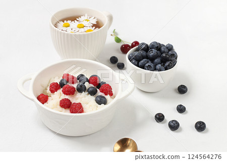 Healthy breakfast with ingredients, milk rice porridge with fresh blueberries, cherries and raspberries, creamy rice pudding or French rice with honey and chamomile tea. Natural nutrition concept, 124564276