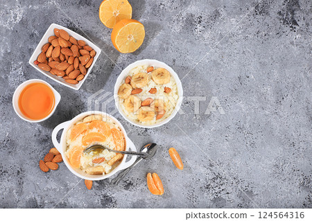 Useful breakfast with ingredients, flat lay, rice pudding with bananas, honey, tangerines and almonds on a sunny table. Healthy and natural food concept, lifestyle, food for children, selective focus 124564316