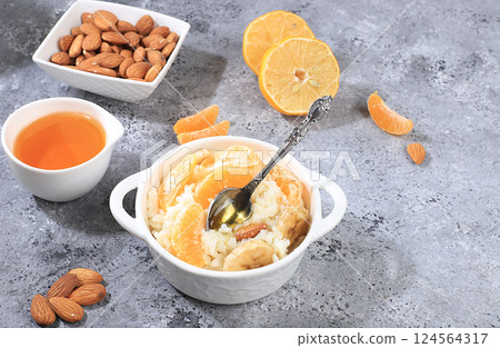 Useful breakfast with ingredients, flat lay, rice pudding with bananas, honey, tangerines and almonds on a sunny table. Healthy and natural food concept, lifestyle, food for children, selective focus 124564317