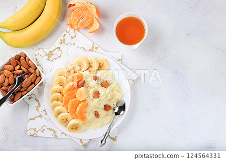 Healthy breakfast with ingredients, flat lay, rice pudding with bananas, honey, tangerines and almonds on a sunny table. Healthy and natural nutrition concept, lifestyle, nutrition for children 124564331