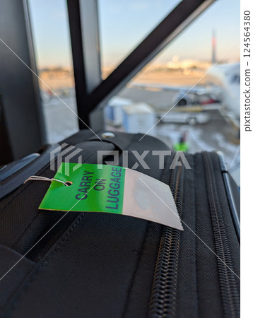 Gate check luggage tag on a roller suitcase in an airport. 124564380